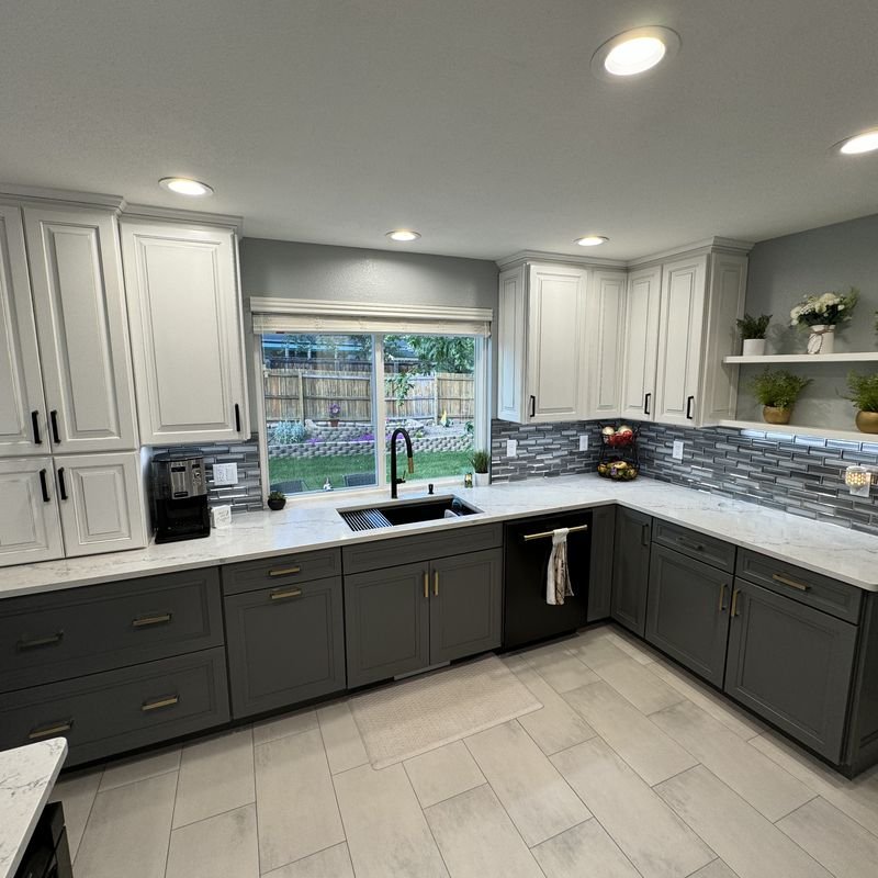 A finished two-tone kitchen with white raised-panel wall cabinets above charcoal base cabinets and brass pulls