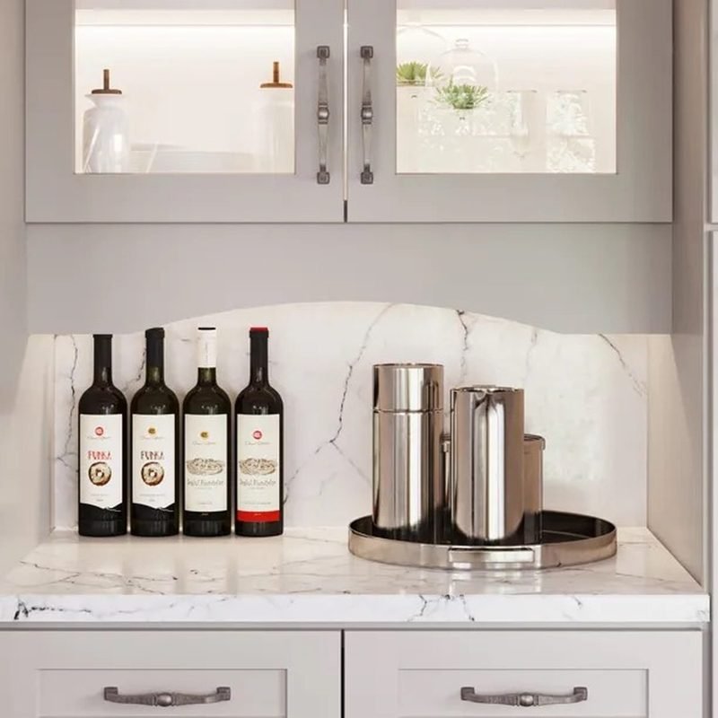 A lit glass-front cabinet above a marble bar counter set with wine bottles and a polished steel tray
